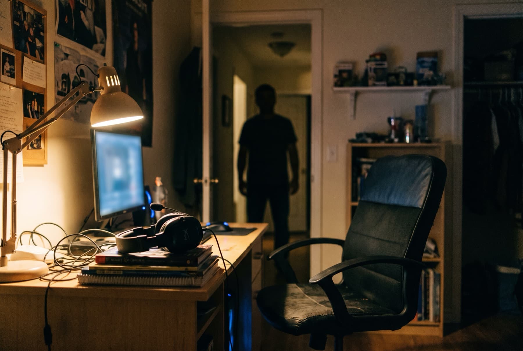 A teenager's bedroom desk at night with a gaming headset and a glowing monitor out of focus