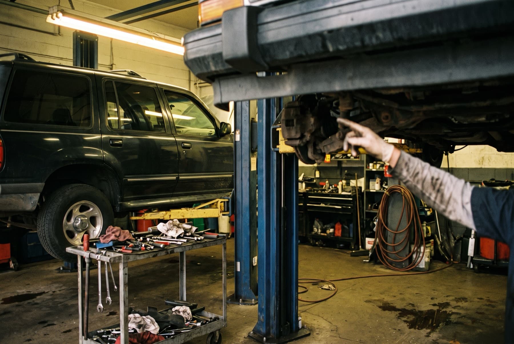 An auto repair shop bay with an SUV on a lift