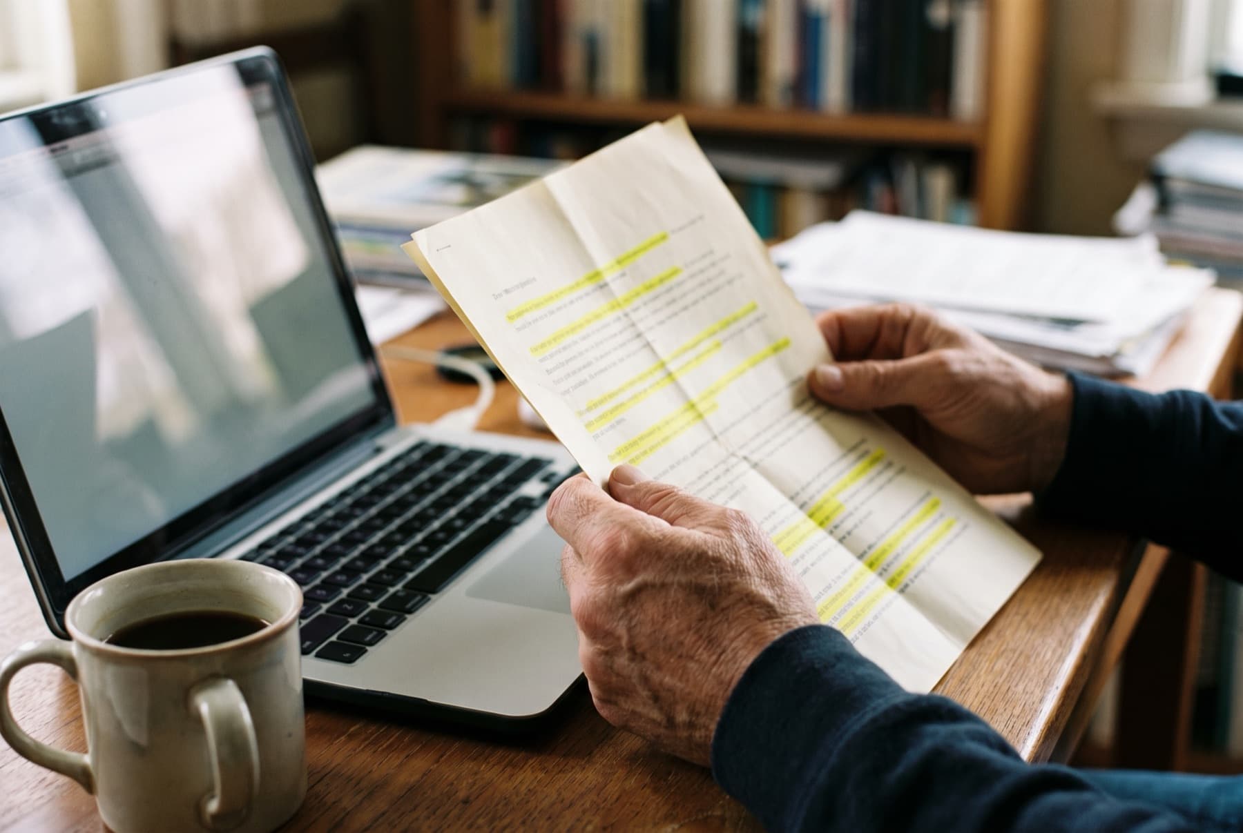 Close view of hands holding a folded credit report next to a laptop and a mug