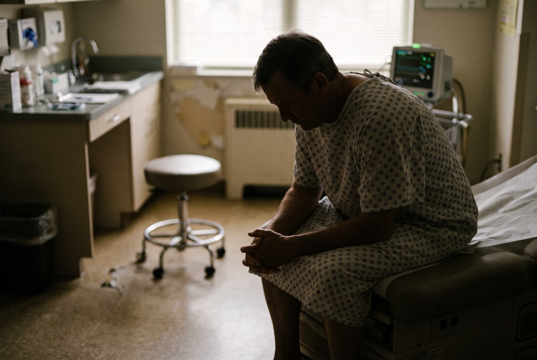 A patient in a hospital gown sitting on the edge of an exam table in a clinic room