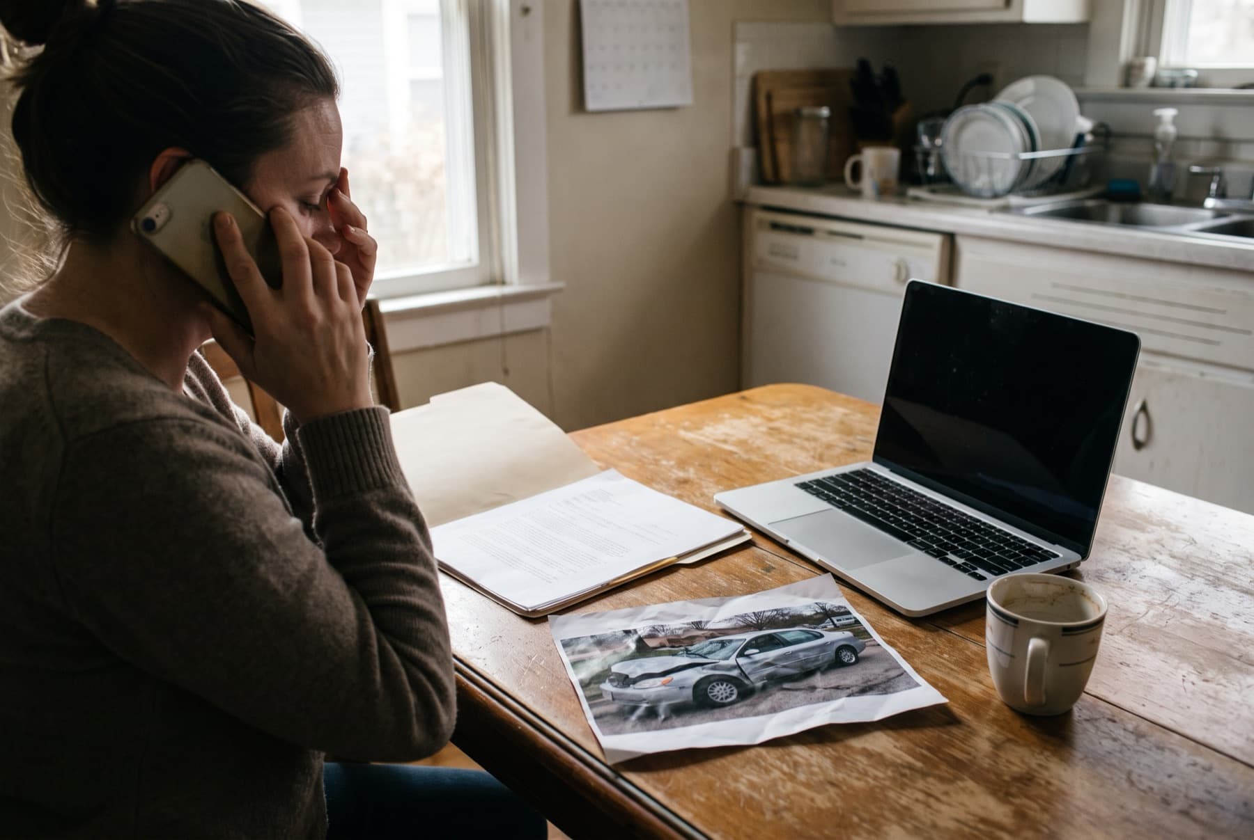 A woman on a phone call at her kitchen table with an insurance claim packet