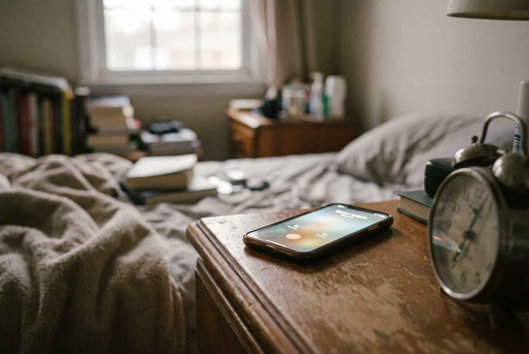 A phone lying on a wooden nightstand lighting up with an incoming call from an unknown number at dawn