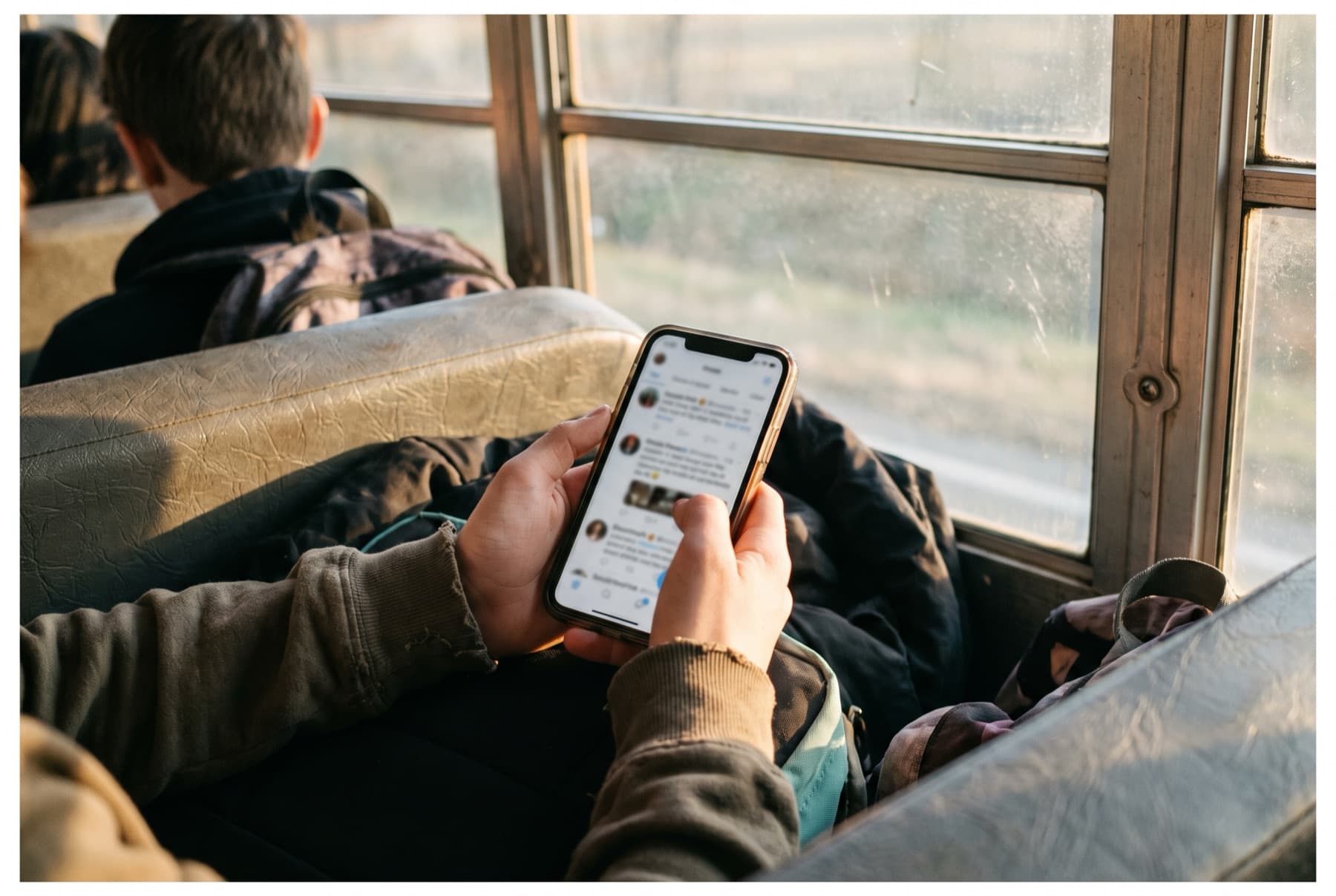 Close view of a teenager's hands holding a phone with a blurred social media feed
