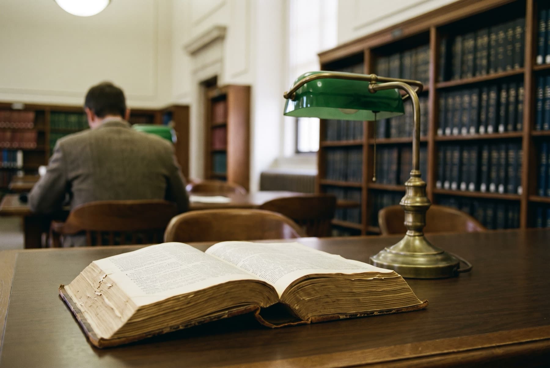 A worn law dictionary open on a library table with a brass lamp