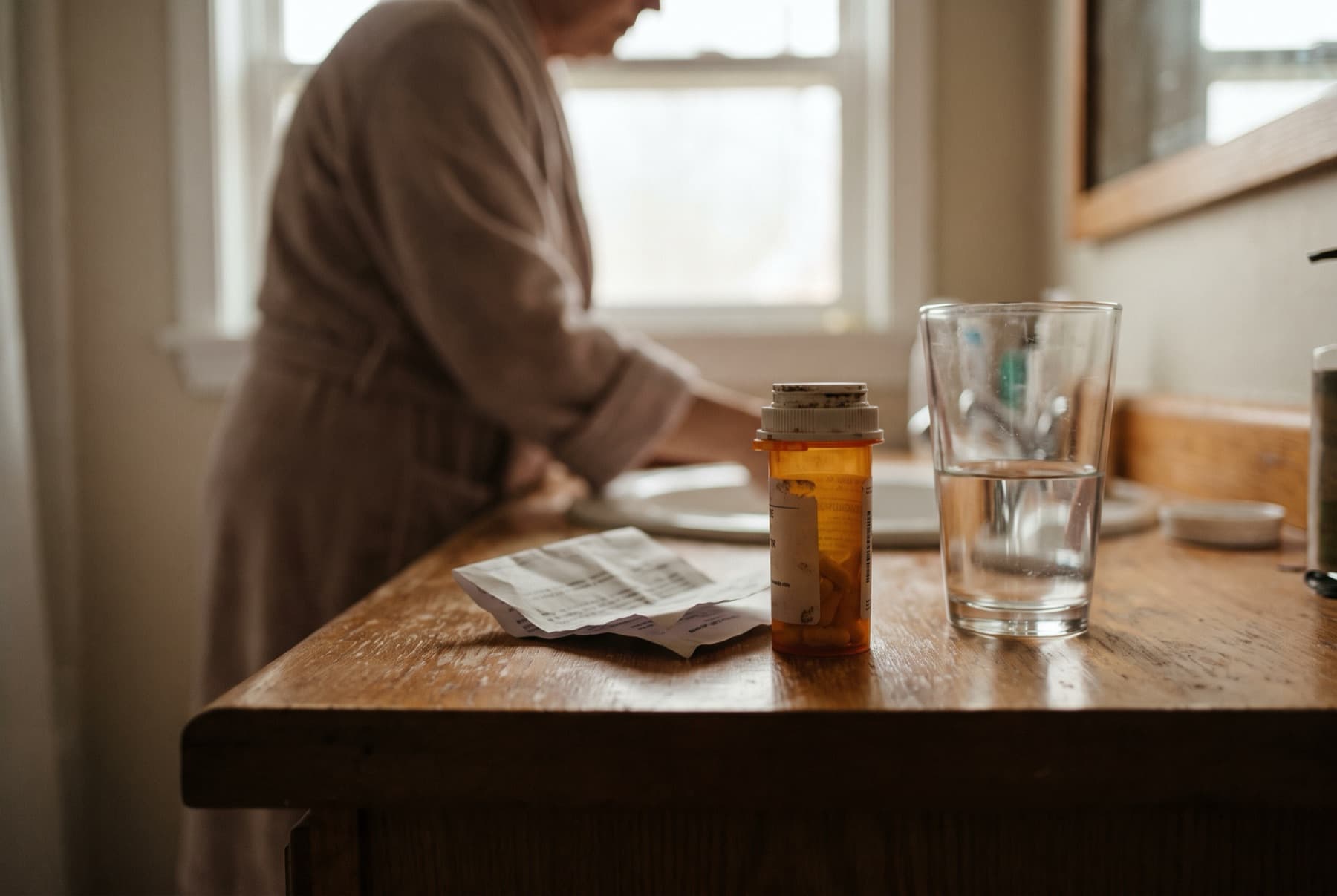 An amber prescription bottle and a folded pharmacy information sheet on a bathroom counter beside a glass of water
